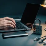 Ontwikkelaarhanden boven laptoptoetsenbord met gesloten combinatieslot en ethernetkabels op bureau, verlicht door warm amberkleurig bureaulampje.