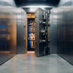 Zware stalen kluisdeur op een kier met zichtbare serverracks en kabelwanden in een modern datacenter, verlicht door warm barnsteenlicht.