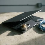 Halfopen laptop op betonnen bureau met combinatieslot op toetsenbord en gerolde netwerkkabel, dramatische zijverlichting.