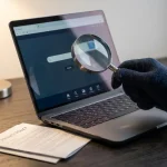 Gehandschoende hand met vergrootglas boven laptop met website, privacybeleid document op donker bureau.
