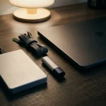 Externe harde schijf en versleutelde USB-stick op donker bureau met kabelorganizers en gesloten laptop, blauwe ledverlichting.