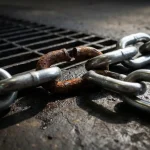Roestige, verzwakte schakel in een verder intacte stalen ketting op een donker industrieel oppervlak.