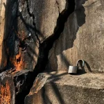 Gebarsten betonnen muur met brandschade aan één kant en een open hangslot op gladde steen aan de andere kant.