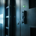 Gebarsten beveiligingsslot op serverruimtedeur met groen "secure" indicatielampje dat nog brandt ondanks zichtbare inbraak.