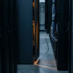 Serverrack met licht openstaand paneel waaruit warm amber licht lekt in een donkere datacentergang, één losse kabel zichtbaar.